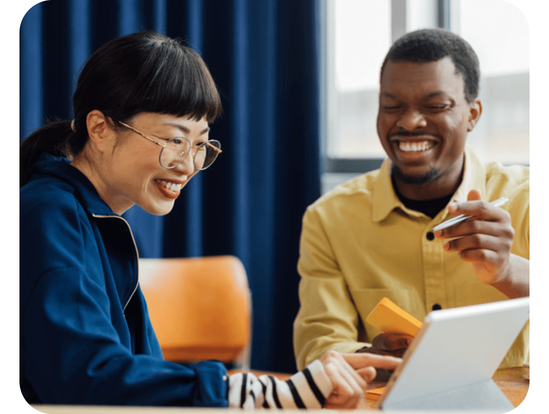 A photo of two colleagues smiling while looking at a laptop