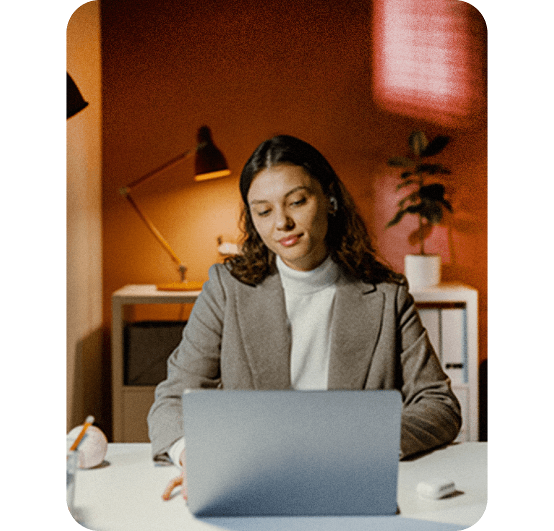 A photo of a woman smiling while looking at a laptop