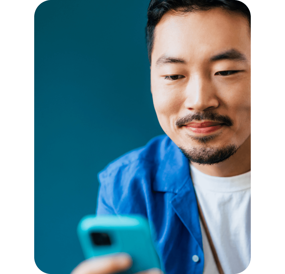 A close up headshot of a man smiling while looking at a phone